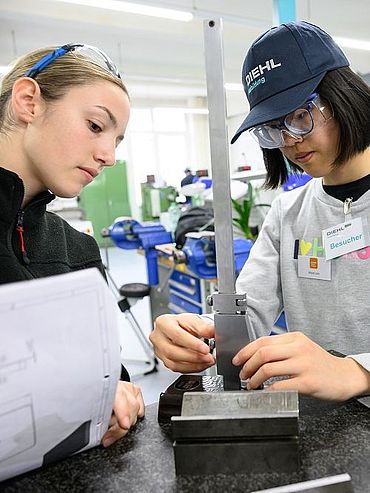 Mädchen für Technik-Camp bei Diehl Ausbildungs- und Qualifizierungs-GmbH Man sieht zwei Auszubildende, die einer Teilnehmerin dabei zuschauen, wie sie etwas misst.