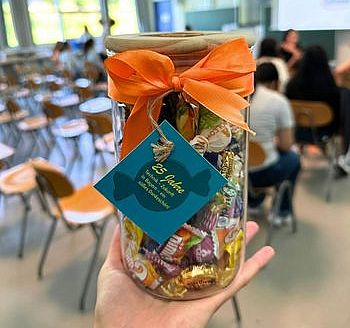 Titelbild_25_Jahre_TeZBa Eine Hand hält ein Bonbonglas mit orangener Schleife und türkisen Label.
