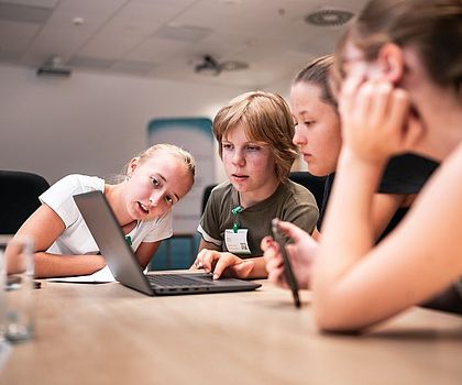 4 Mädchen sitzen vor einem Laptop und arbeiten