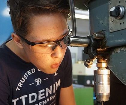 Ein Junge bohrt an einer Standbohrmaschine Löcher in eine Metallplatte