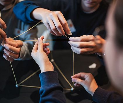 6 Hände versuchen Spaghetti zu einen Viereck zu formen