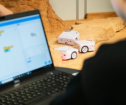 Person programmiert kleine Roboter mit grafischer Software vor einer Testlandschaft.