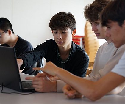 3 Jungen sitzen vor einem Laptop. Sie versuchen gemeinsam einen Code zu schreiiben