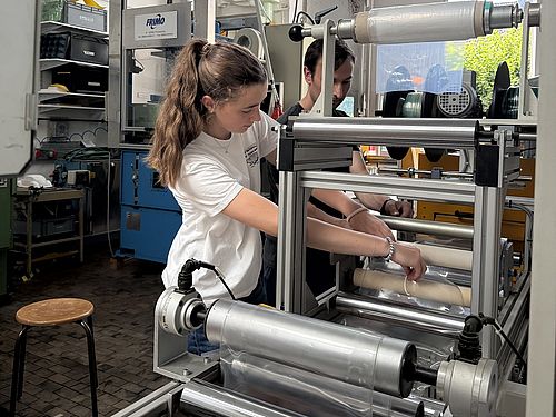 Eine Jugendliche bedient gemeinsam mit einem Betreuer eine Rollenmaschine zur Folienverarbeitung.