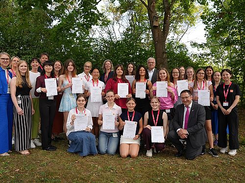 Gruppenfoto der Camp-Teilnehmerinnen mit ihren Urkunden sowie Vertreterinnen und Vertretern von Infineon, der OTH Regensburg und der Politik im Grünen.