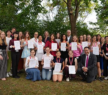 Gruppenfoto der Camp-Teilnehmerinnen mit ihren Urkunden sowie Vertreterinnen und Vertretern von Infineon, der OTH Regensburg und der Politik im Grünen.