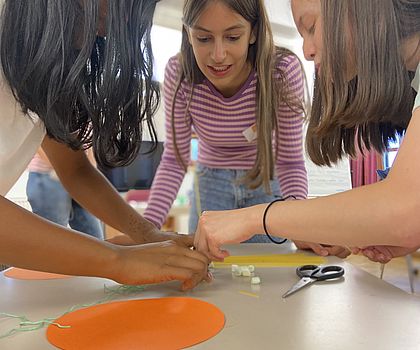 Drei Mädchen haben die Köpfe zusammengesteckt und blicken auf den Tisch. Sie arbeiten an etwas gemeinsam.