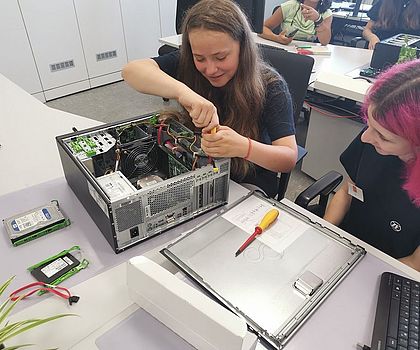 2 Mädchen sitzen vor einem PC und nehmen diesen auseinander