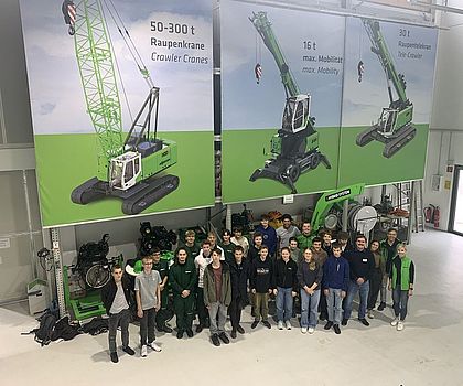Gruppenbild von oben der Teilnehmenden und im Hintergrund sind Kräne als riesen Poster zu sehen. 