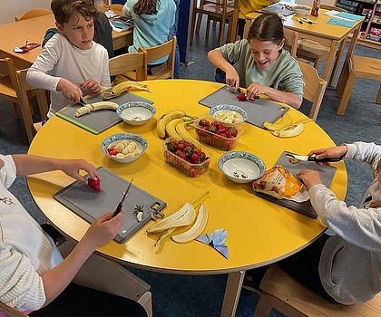 Auf dem Foto sind Kinder zu sehen, die an einem runden Tisch sitzen und Essen zubereiten.
