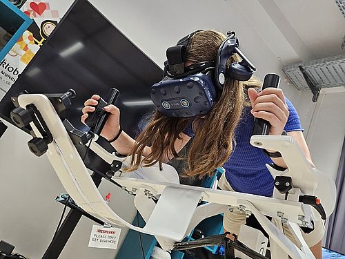 Eine Jugendliche nutzt ein VR-Headset auf einem neigbaren Bewegungssimulator.