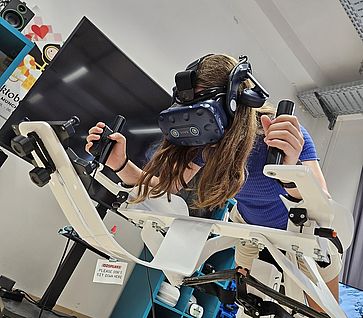 Eine Jugendliche nutzt ein VR-Headset auf einem neigbaren Bewegungssimulator.