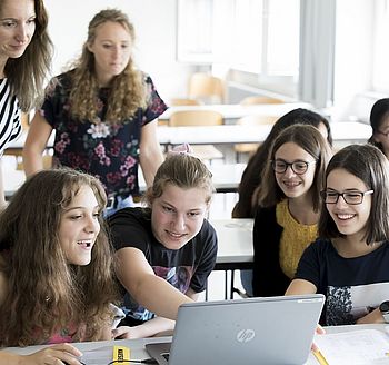 Man sieht mehrere Mädchen, die freudig auf einen Laptop in der Mitte zeigen. 