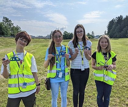 4 Mädchen stehen auf einer Wiese. Jede hält einen Mini-Helikopter in der Hand.