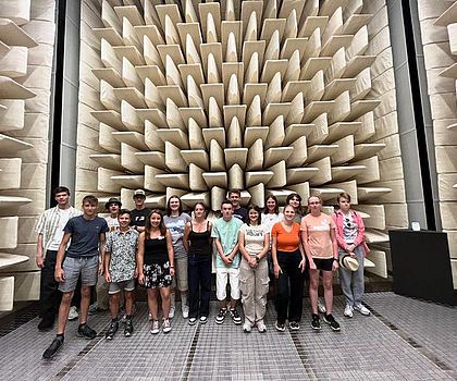Die Gruppe steht in einem Raum mit Platten an der Wand, die die Akustik verändern. 