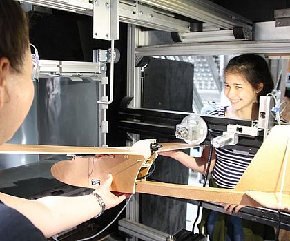 2 Mädchen beobachten das Strömungsverhalten bei einem Flugzeug im Windkanal