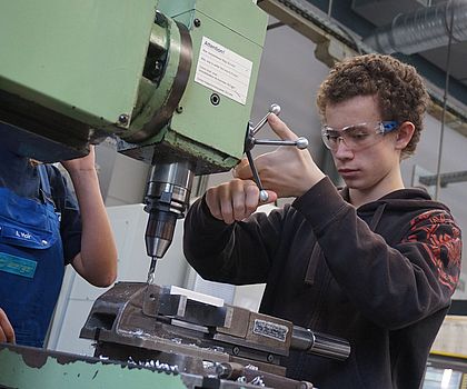 Konzentrierter Junge mit Schutzbrille beim bohren an einer großen Maschine
