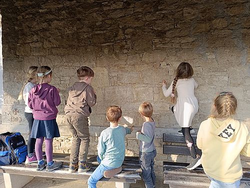 Auf diesem Bild sind Kinder zu sehen, die eine Steinwand betrachten um  Versteinerungen zu finden.