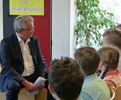 Auf dem Foto ist Herr Brossardt zu sehen, der gegenüber von mehreren Kinder sitzt und mit ihnen spricht.