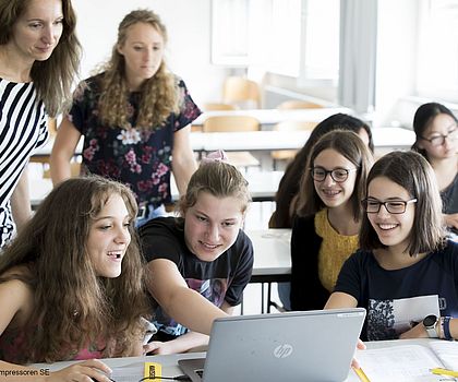 junge Frauen mit fröhlichen Gesichtern sitzen um ein Laptop
