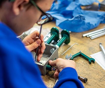 Ein Junge sitzt an einem Tisch und verbaut Teile an den Roboter